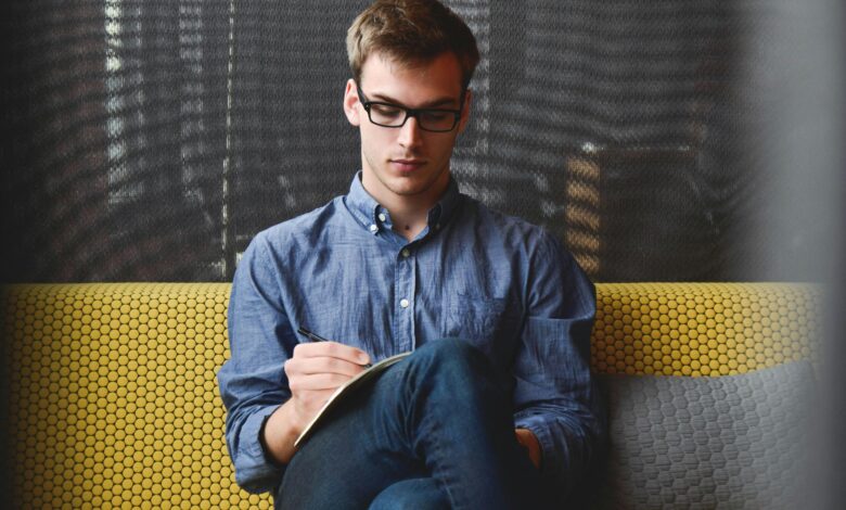 Young man in glasses writes in a notebook.