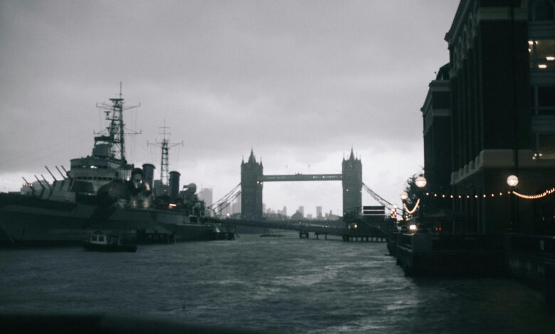 Dramatic black and white photo of Tower Bridge in London with warship and water reflections at dusk.