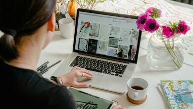 Woman using laptop and tablet in a creative workspace, calligraphy tools nearby. Artistic and tech-driven.