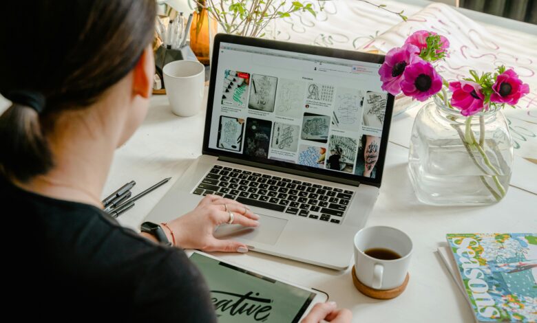Woman using laptop and tablet in a creative workspace, calligraphy tools nearby. Artistic and tech-driven.