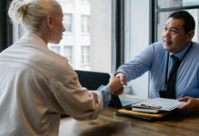 Two professionals in an office setting shaking hands after a business agreement.