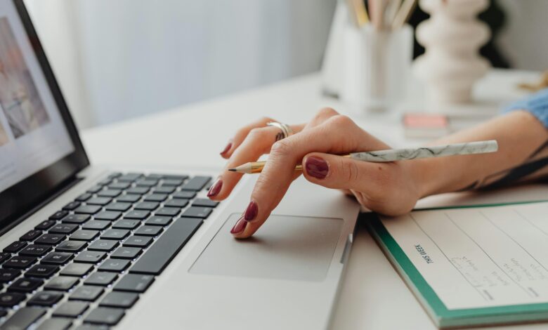 Person typing on laptop, notebook and pen nearby, crafting a post-interview email.