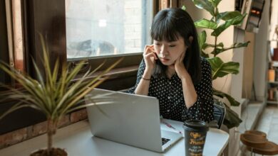 Asian woman focused on work in a modern office with laptop and coffee.