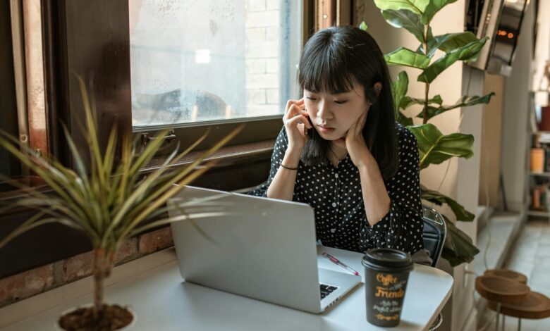 Asian woman focused on work in a modern office with laptop and coffee.
