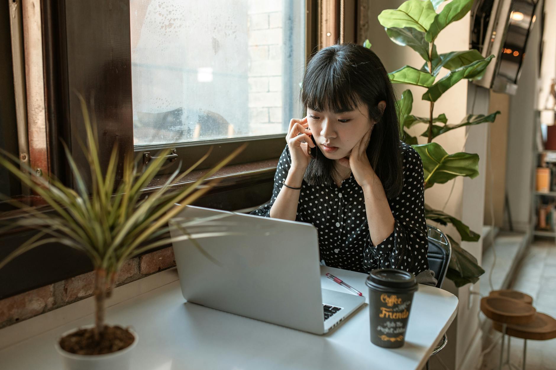 Asian woman focused on work in a modern office with laptop and coffee.