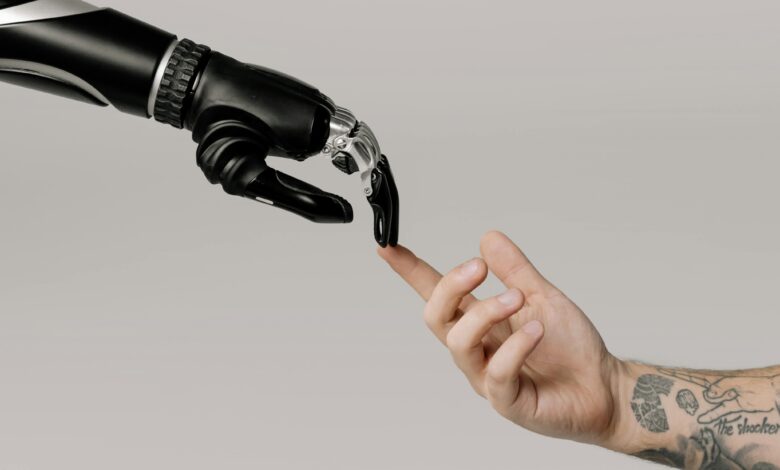 A human hand with tattoos reaching out to a robotic hand on a white background.