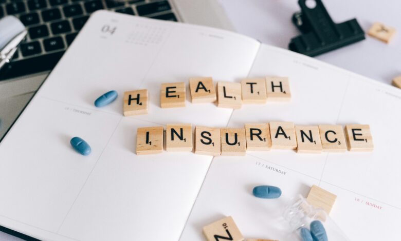 Scrabble tiles spelling 'Health Insurance' on planner with pills and laptop, symbolizing healthcare planning.