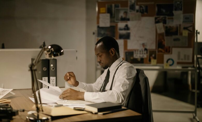 Man in office reviewing documents under desk lamp, late hours.